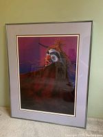 Framed print artwork showing a person wearing a traditional Indigenous mask with detailed patterns and natural elements like feathers, dominated by purple and red background.