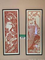 Frontal view of two framed Jianzhi style paper cuttings hung on wall with detailed red designs of cranes and peacock