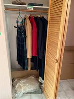 Photo showing a closet with a Campbell of Argyll tartan kilt, three wool coats in beige, red, and navy colors hanging on hangers, a pair of shoes on top shelf, and items in a box below.