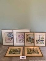 Photo of six framed prints including 4 Marius Girard Paris landmark prints and 2 floral hydrangea prints, arranged on carpet.