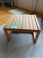 Side angle view of the pine wood slatted end table placed on a beige rug, showing the table's thickness and construction.