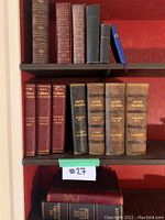 Six decorative volumes on top shelf: brown leather, two burgundy “Books” volumes, dark green cloth, black cloth, small blue.