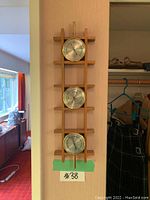 Full view of the vertical wooden frame holding three circular metal dials mounted on a light-colored wall.