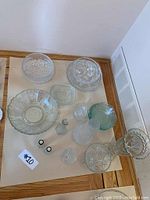 Full view of vintage pressed glass collection items spread on table showing various shaped bowls, vases, decanter, and smaller dishes.