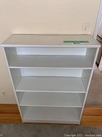 Front view of white wooden shelf unit showing four shelves and overall condition