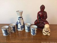 Full lot image showing the sake set and both Buddha figurines on wooden surface with neutral wall background.