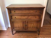 Closed front view of wood veneer cabinet showing two drawers with brass knobs above double panel doors.