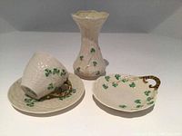 Set of porcelain items including tea cup with saucer, oval dish with basket handle, and vase all featuring shamrocks and basketweave texture.
