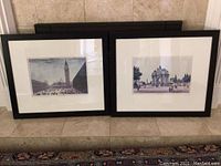 Pair of framed art prints displayed on floor against wall, black frames with white mats