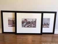 Three framed vintage-style cityscape prints leaning against a wall, arranged partially overlapped.