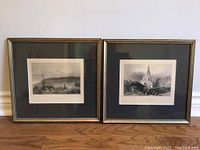 Two framed black and white prints leaning against white wall on wooden floor, showing the front view