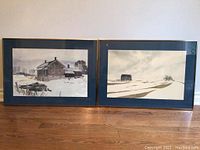 Two framed watercolor paintings by Robert J Anderson, showing various winter scenes, displayed side by side on a hardwood floor.