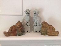 Two white ceramic foo dogs sitting on pedestals with spherical balls and two reclining wooden child figurines holding spherical objects.