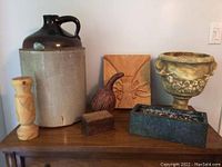 Front view showing large ceramic jug, wooden candlestick holder, wooden gourd carving, wooden box, wood carved plaque, and two metal planters on wooden surface.