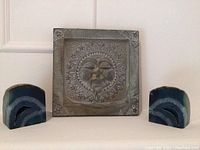 Photo of carved natural stone plate with sun face and two blue agate bookends on either side.