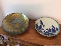 Two decorative platters on wooden side table, one glass with leaf design, one ceramic with blue and white pattern