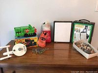 Full lot view including green plastic toy vehicles, Star Trek ship, box of rocks, kite kit, and polystyrene board