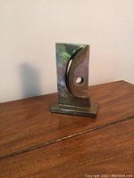 Front angled view of the abstract metal sculpture showing crescent shape and patina.