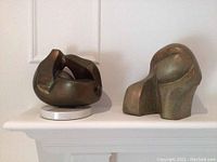 Photo showing two abstract bronze sculptures displayed on a white surface, highlighting their forms and relative size.