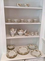 Wide view showing multiple pieces arranged on shelves including cups, plates, teapot, coffee pot, sugar bowl, creamer, and handled bowls.