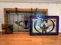 Three stained glass panels arranged on floor: large rectangular with floral motif, medium rectangular floral panel, small geometric square panel