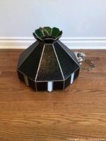 Top and side view of dark green textured stained glass hanging light shade with white vertical accents on bottom edges, metal framing, chain, and canopy