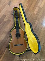 Overhead view of guitar seated in open black hard shell case lined in yellow plush, showing body and interior condition