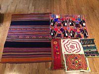 Full view of all textile items laid out on a wood floor showing multiple colorful woven and embroidered fabrics, including large tapestry.