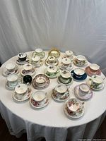 Top-down view of 22 matching cups and saucers with various floral patterns and colors on a white cloth.