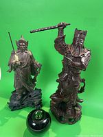 Photo showing both carved Chinese hardwood warrior figurines with a green glass apple for size reference.