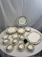 Full set of Coalport Maytime 29-piece dish set arranged on a table with cups, saucers, and plates of various sizes. Small green apple for size reference.