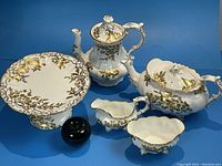 Overview of entire set on blue background showing coffee pot, teapot, creamer, sugar bowl, and cake stand
