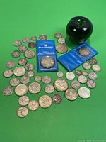 Assortment of Canadian silver coins including silver dollars in protective sleeves, quarters, dimes and nickels with a green apple for scale