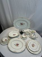 Overview of set arranged on table with large platter on stand, platters, plates, cups, saucers, creamers, sugar bowl and serving bowls