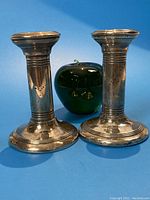 Two sterling silver column-form candlesticks with a green apple for size reference, shown against blue background