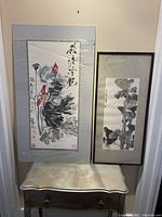 Both framed paintings leaning against wall on console table