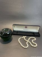 Full view of pearl necklace laid in front of open black presentation box showing Union Jack emblem.