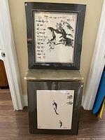 Both framed paintings leaning against a wall, top and bottom arrangement