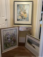 Three framed watercolor paintings displayed together: cream peony still life, purple irises, and snowy landscape