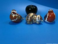 Three painted porcelain paperweights and green apple reference on blue background