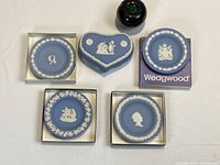 Top view of four round dishes and one heart-shaped ring box, all on flat surface, some still in original Wedgwood boxes. Includes black glass item and green apple for size reference, not part of lot.