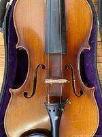 Front view of violin inside case showing spruce top, f-holes, fingerboard, bridge and tailpiece