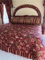 Full view of bed with floral bedspread, matching curtains, vertical striped bed skirt, and specialty bolster pillow.