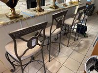 Four heavy duty metal framed bar stools with cushioned cloth seats lined up next to a granite countertop.