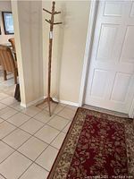 View of wooden hall tree standing near wall, showing its height, twisted column, and tripod base with multiple hooks at top.