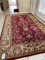 Full view of the rectangular red and beige floral area rug on tile floor near entrance door.