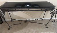 Full front view of the console table showing black granite top and metal base with scroll legs.