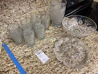 Glass pitcher, six glasses, bowl, and serving platter displayed on granite countertop showing details of cut glass pattern.