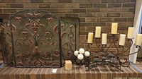 Full photo of entire lot showing fireplace screen and two candle holders with candles in front of a brick fireplace