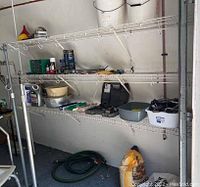 Wide view of wire shelving unit holding assorted garage items including Ryobi drill, electronic wires in bins, lightbulbs, sealants, and small paint cans.
